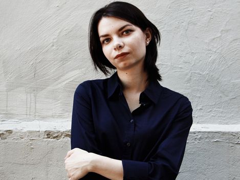Young woman with dark hair standing against a light textured wall with arms crossed in front of her chest.