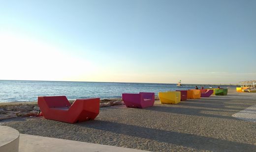 Colorful Enzi seating modules line a seaside promenade, facing the sea and the horizon.