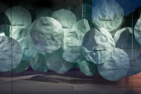 Close-up of the installation “EMOTION” showing densely arranged floating turquoise face-like forms inside the space.