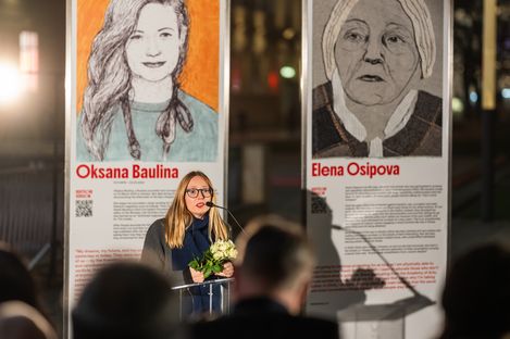 Eröffnung der Installation Women Against War, 2025. Eine Frau hält eine Rede vor den Ausstellungsplakaten vor einem Publikum.
