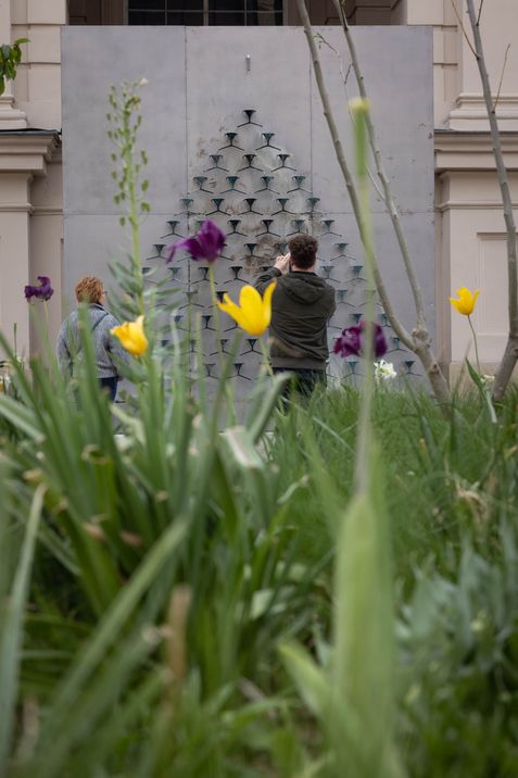Visitors observing Pavlo Makov’s “Fountain of Exhaustion,” with flowers in the foreground.