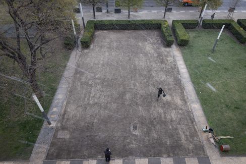 Two people stand on a rectangular bare area bordered by low hedges.