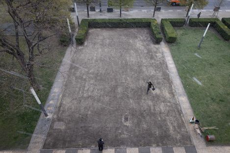 Two people stand on a rectangular bare area bordered by low hedges.