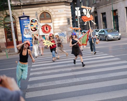 Group of people wearing colorful costumes and holding signs crossing a city crosswalk