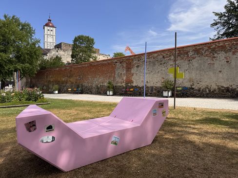 Draufsicht auf zwei Frauen, die entspannt auf einem rosa Enzi liegen. Sie tragen weiße Socken und halten Getränke in der Hand, während sie den Sommertag im Schlosspark Schallaburg genießen.