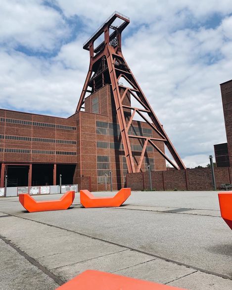 Orangefarbene Enzi-Sitzmöbel stehen auf einem Platz vor der Industriearchitektur der Zeche Zollverein.