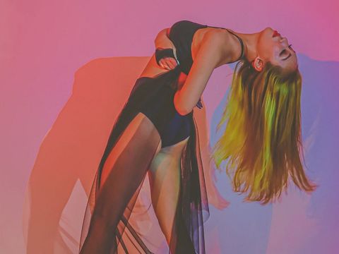 Woman in black sheer dress leaning backward against pink background