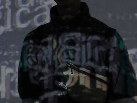 Silhouette of a standing person against a wall with partially legible projected text fragments.