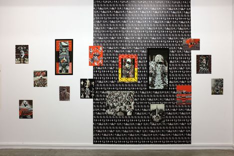 Wall installation with multiple small rectangular collages and photographs arranged on a large black-and-white patterned background.
