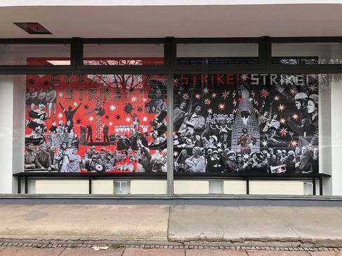 Store window with a black-and-white collage of historical photos showing people at strike actions on a red background with the text "EVERYBODY STRIKE".