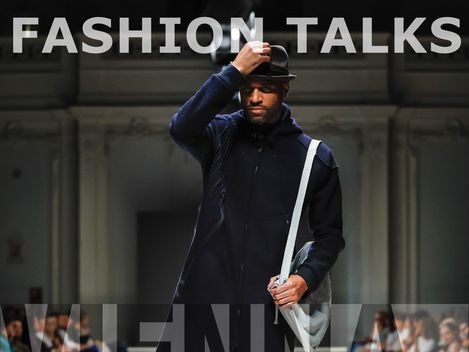 Man in dark clothing and hat walking on runway with audience on both sides, text "FASHION TALKS" and "WIENER FASHION WEEK" overlaid.
