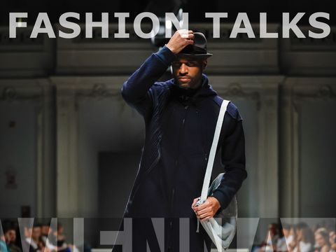 Man in dark clothing and hat walking on runway with audience on both sides, text "FASHION TALKS" and "WIENER FASHION WEEK" overlaid.