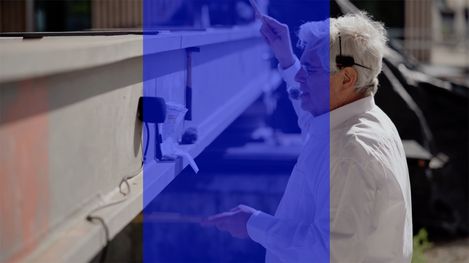 An older man in a white shirt stands sideways by a concrete bridge holding a rod.