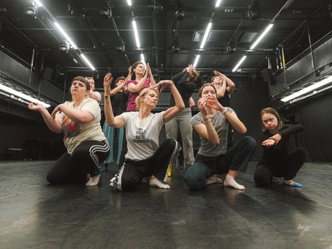 Tänzerinnen und Tänzer sind in einer choreografierten Pose abgebildet.