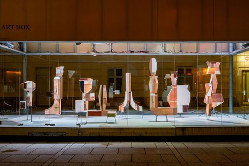 Art display featuring abstract wooden sculptures in varying geometric shapes, set in a brightly lit glass case against a dim backdrop, exuding modern elegance.