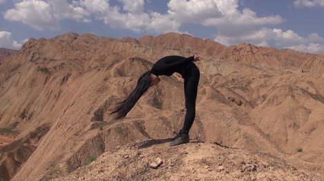Person dressed in black bending backward over a rocky hill in a mountainous landscape.