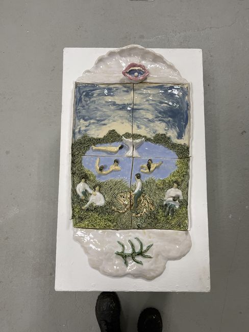 Ceramic relief depicting a landscape with a lake, people in various poses, and a large open lip at the top edge.