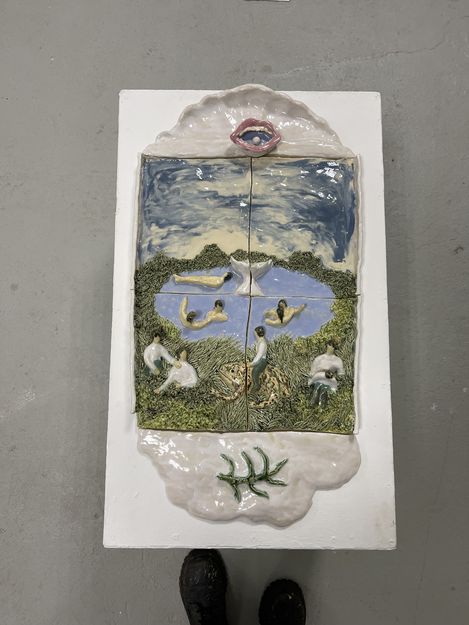 Ceramic relief depicting a landscape with a lake, people in various poses, and a large open lip at the top edge.