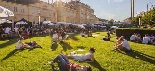 Menschen sitzen und liegen auf einer Wiese vor dem MQ und lassen sich sonnen.