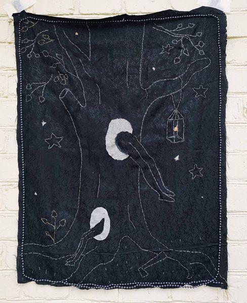 Textile wall hanging showing a large tree with two hollow trunks each with a leg sticking out, surrounded by stars and a hanging lantern motif.