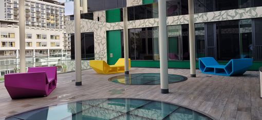 Mehrere farbige Enzos als Sitz- und Liegeelemente in einem modernen, überdachten Innenhof mit Glasflächen und Säulen.