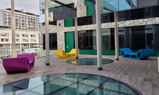 Several colorful Enzo seating and lounge elements placed in a modern covered courtyard with glass surfaces and columns.