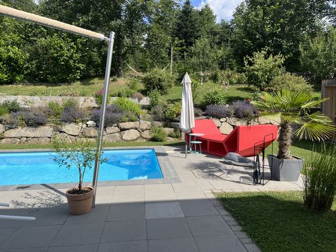 Roter Enzo als Sitz- und Liegeelement neben einem privaten Pool in einem begrünten Garten.