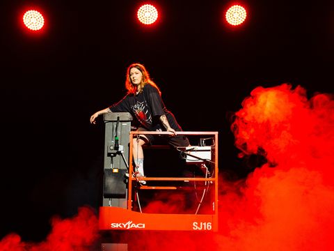 Eine Bühnentechnikerin steht auf einer Hebebühne, die Genie genannt wird. Sie ist von Nebel umhüllt, der in rotes Licht getaucht ist.