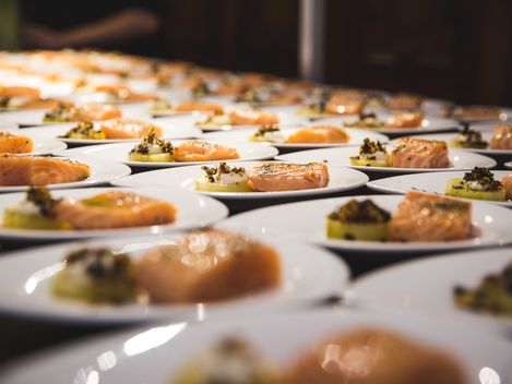 Viele schön angerichtete kleine Teller mit Lachs und Beilagen.