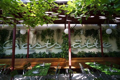 Covered outdoor dining area with wooden benches, green tables, metal chairs, and lush plants on the wall and pergola.
