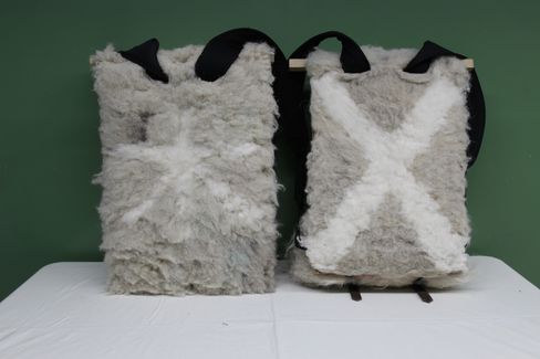 Two rectangular backpacks covered in fluffy light gray material with white X patterns, front and back visible, with black shoulder straps.