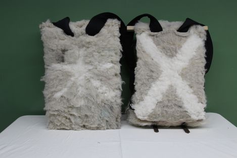 Two rectangular backpacks covered in fluffy light gray material with white X patterns, front and back visible, with black shoulder straps.