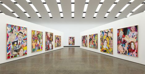 Multiple colorful paintings with portraits and abstract patterns hang on the white walls of a large, modern exhibition hall.