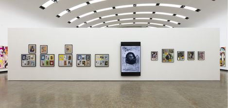 An art exhibition featuring five colorful collages composed of many small portraits and figures, hanging in front of a large-format, abstract black-and-white painting.
