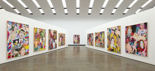 Multiple colorful paintings with portraits and abstract patterns hang on the white walls of a large, modern exhibition hall.
