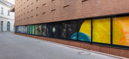 Bunte Gemäldeinstallation mit gemalten Elementen wie Bäumen und Planeten an einer Ziegelfassade der Kunsthalle Wien.