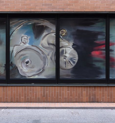 Das Bild zeigt ein großes Fenster mit einem Gemälde von Sophie Hellermann, auf dem eine Person auf einem Fahrrad zu sehen ist, an der Seite der Backsteinfassade der Kunsthalle Wien.