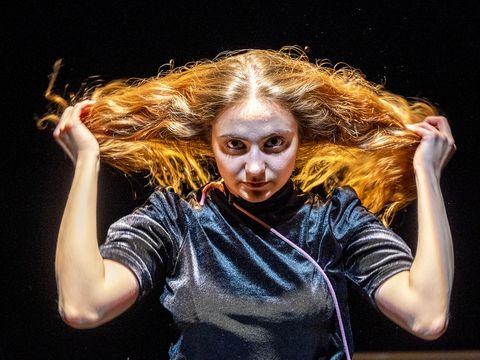 A young woman is holding her long hair in her hands and looking straight into the camera.