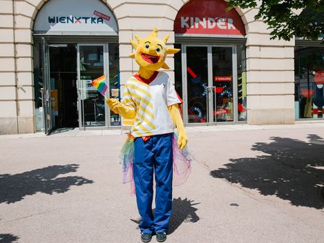 Holli ist standing in front of Kinderinfo with a Pride flag in their hand
