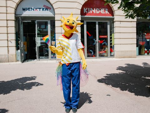 Holli steht vor der Kinderinfo und hat eine Regenbogenflagge in der Hand