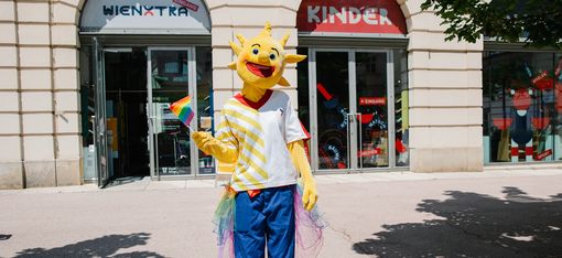 Holli ist standing in front of Kinderinfo with a Pride flag in their hand
