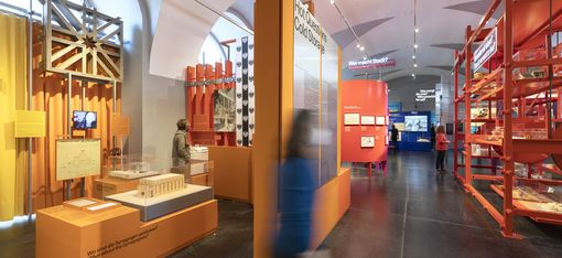 Several people in a room with yellow, orange, and red exhibits and furniture.