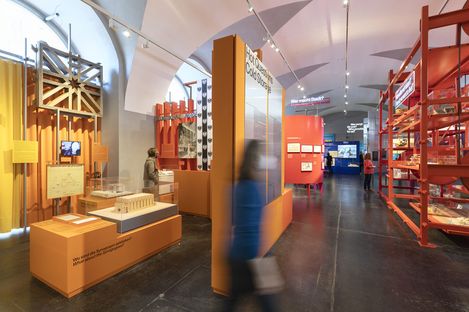 Several people in a room with yellow, orange, and red exhibits and furniture.