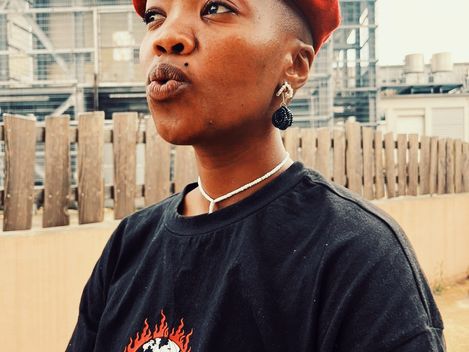 Young person wearing a red beret, black T-shirt with flames and skull design, stud earrings, and necklace in an urban setting