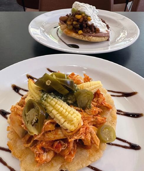 Two tostadas, one with chicken, corn, and jalapeños, the other with beans, ground beef, and sour cream.