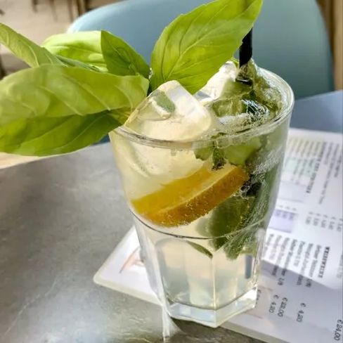 Refreshing lemon soda with basil, ice cubes, and a straw.