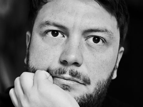 Black-and-white portrait of a person resting their chin on their hand against a dark background.