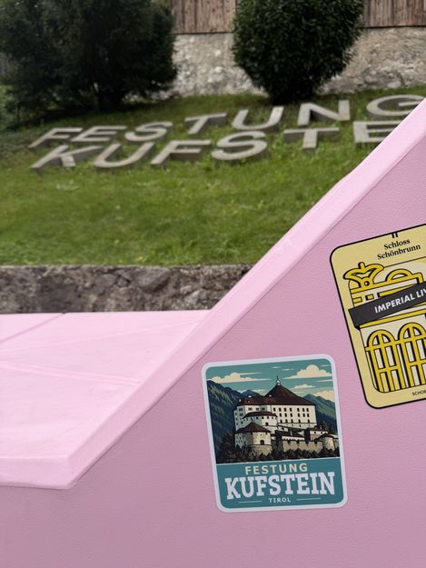 Detailansicht des rosa MQ-Möbels mit Aufklebern der Festung Kufstein und von Schloss Schönbrunn, im Hintergrund der Schriftzug „Festung Kufstein“.