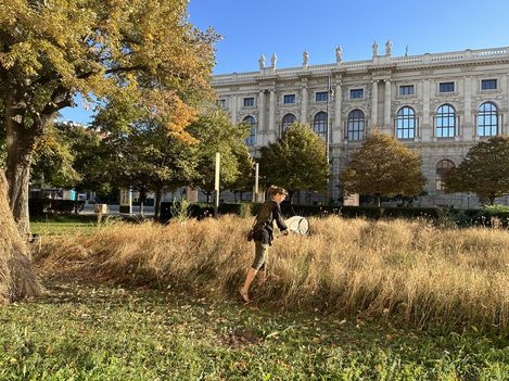 Person with a net stands in tall grass in front of a historic building.