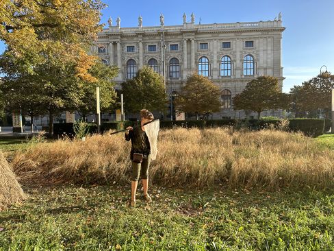 Person with a net stands on a meadow in front of a historic building.